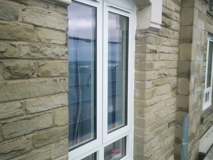 Exterior of a building with beige brick walls and a white-framed sliding glass door, reflecting sky and clouds.
