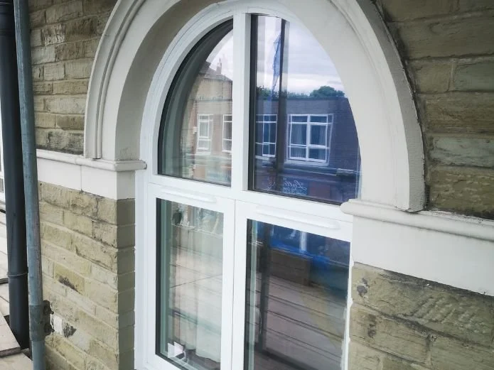 Close-up of a white-framed arched window in a brick building, reflecting neighboring houses with blue and white facades.