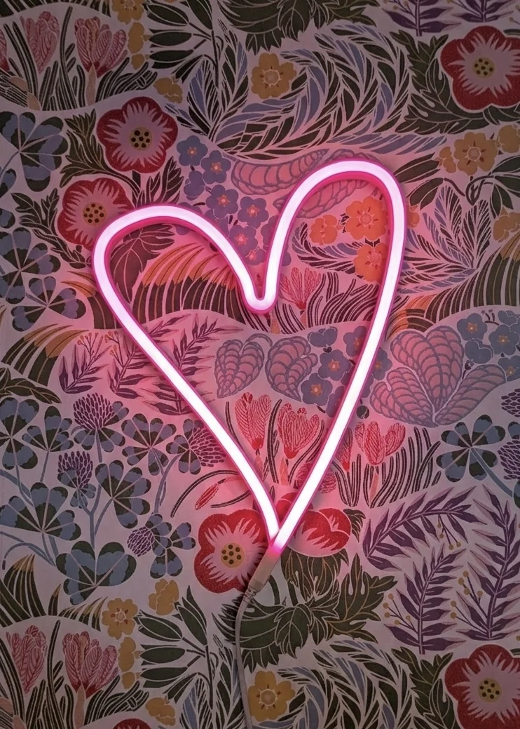 Néon rose fluo d’un coeur rose sur papier peint coloré
