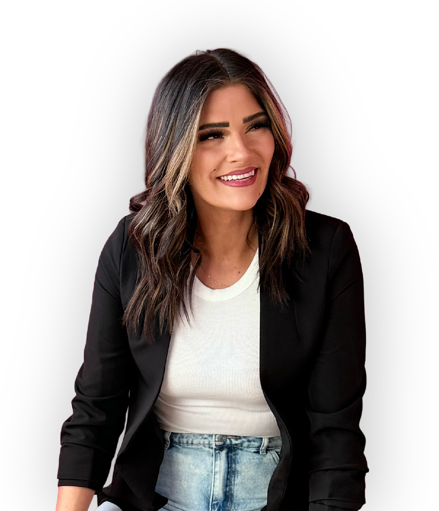 A woman with long brown hair wearing a black blazer, white T-shirt, and light blue jeans, smiling against a black background.