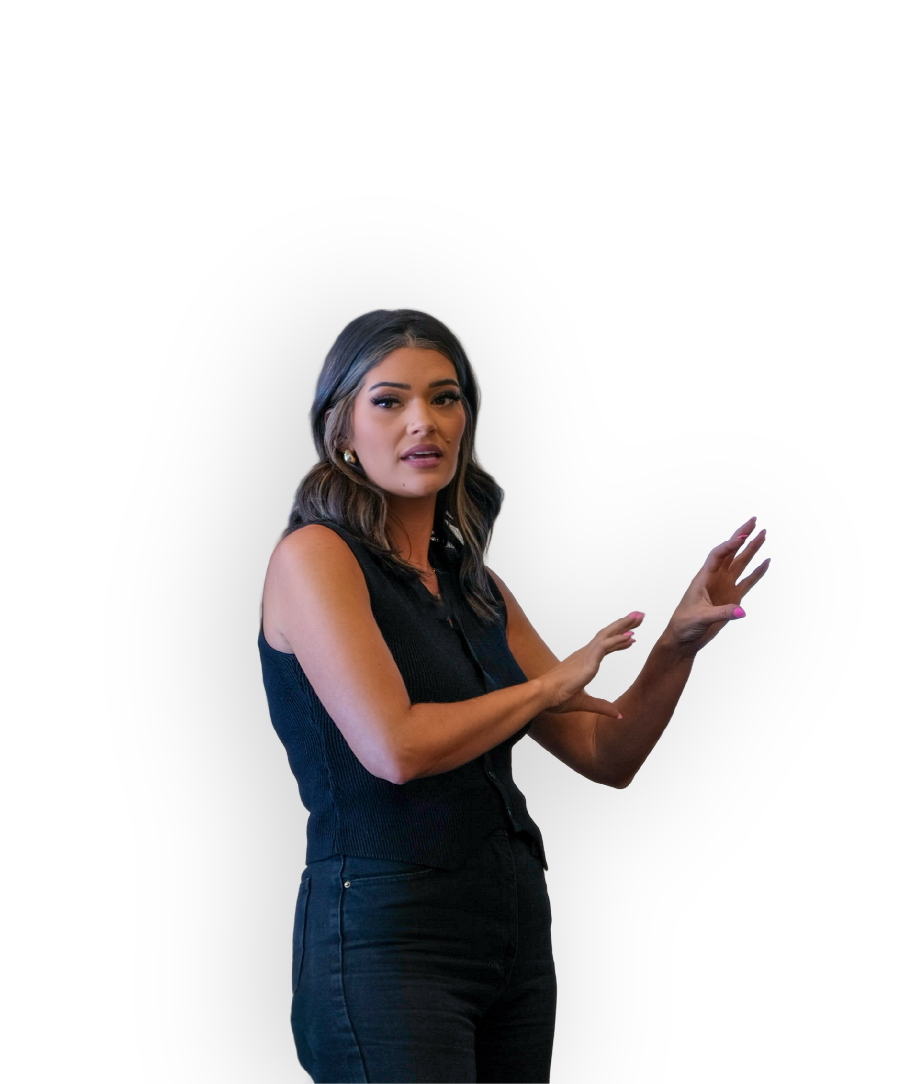 A woman with long, wavy dark hair and makeup, wearing a sleeveless black top, making a hand gesture against a plain black background.