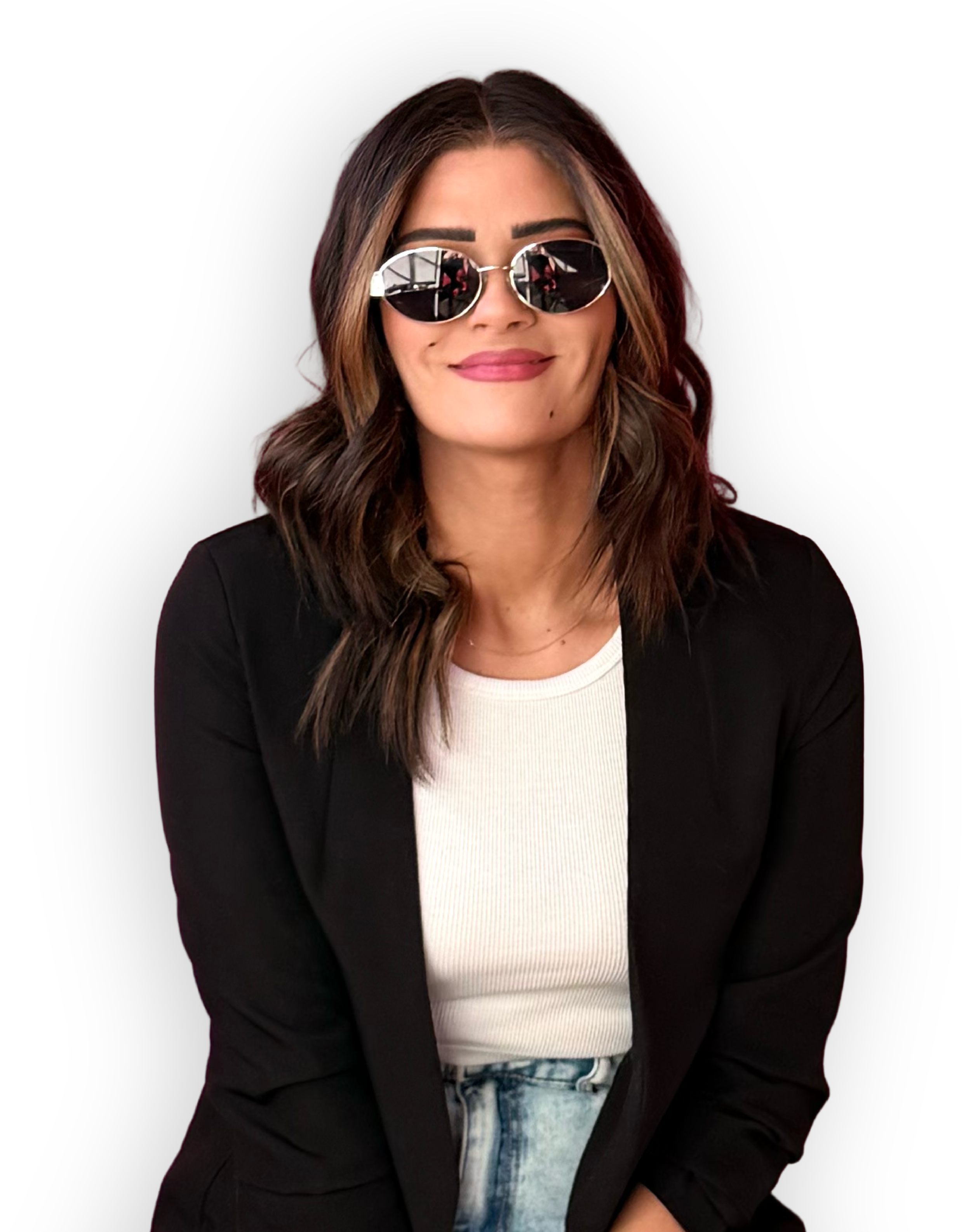A woman wearing sunglasses with round reflective lenses, a black blazer, a white shirt, and tie-dye jeans, smiling with her arms crossed against a black background.