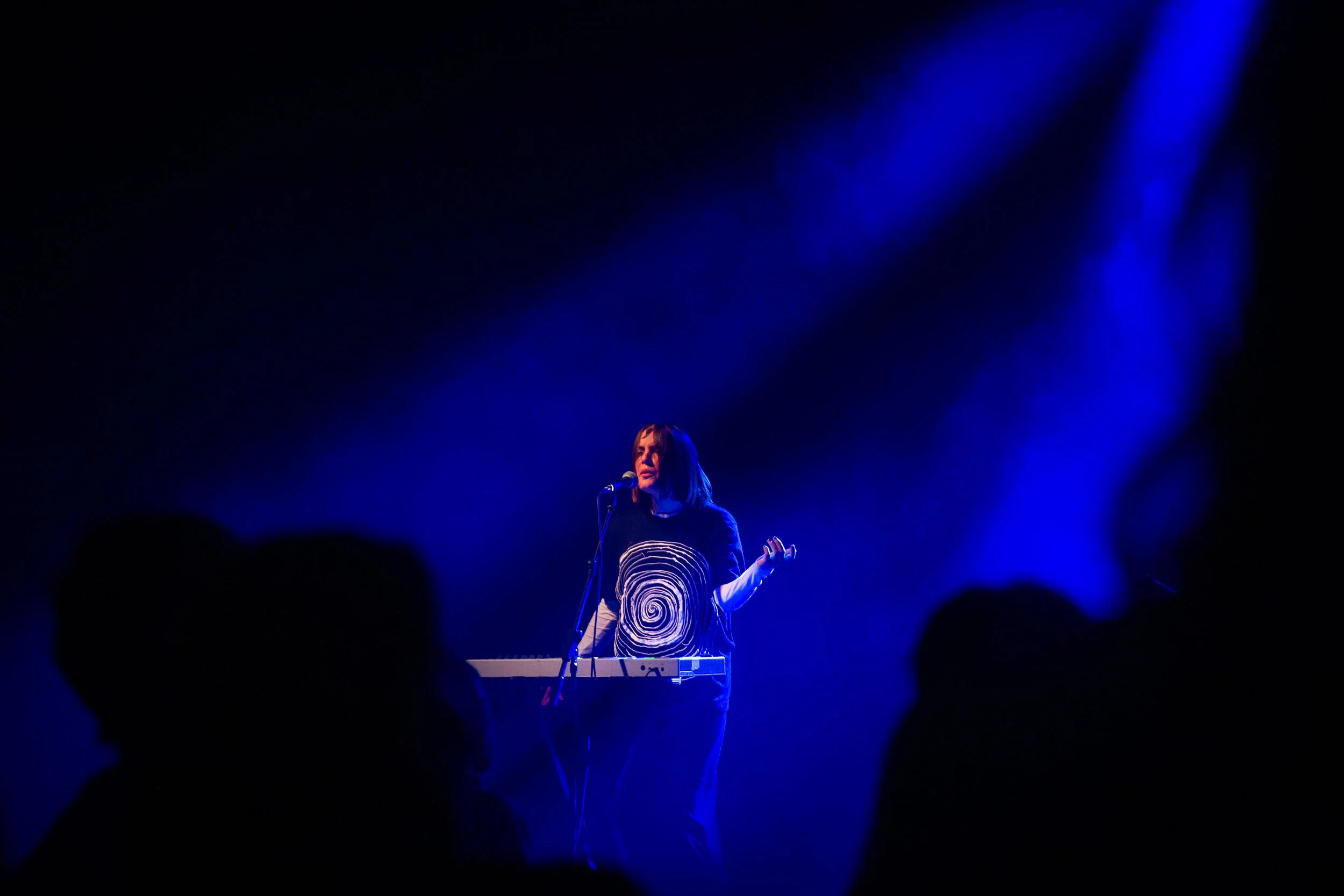 A woman performing on stage with blue lighting and a keyboard, in front of an audience
