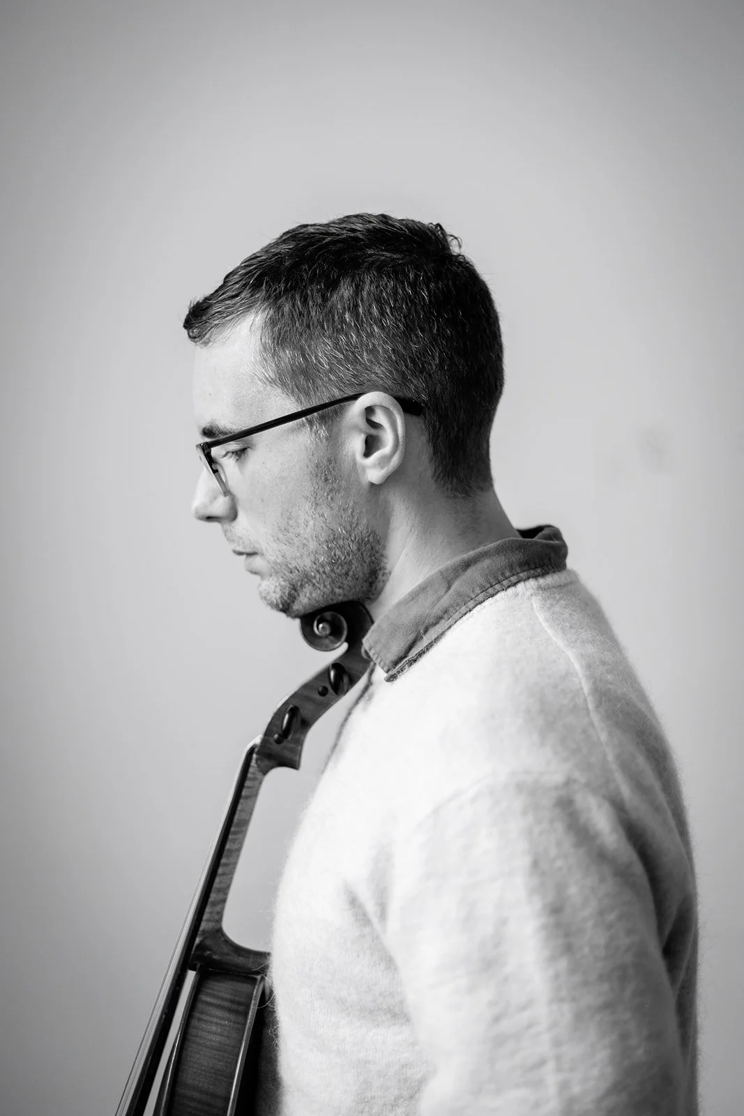 A black and white photo of a man with glasses and short dark hair, looking down, with a pair of headphones around his neck, facing sideways.