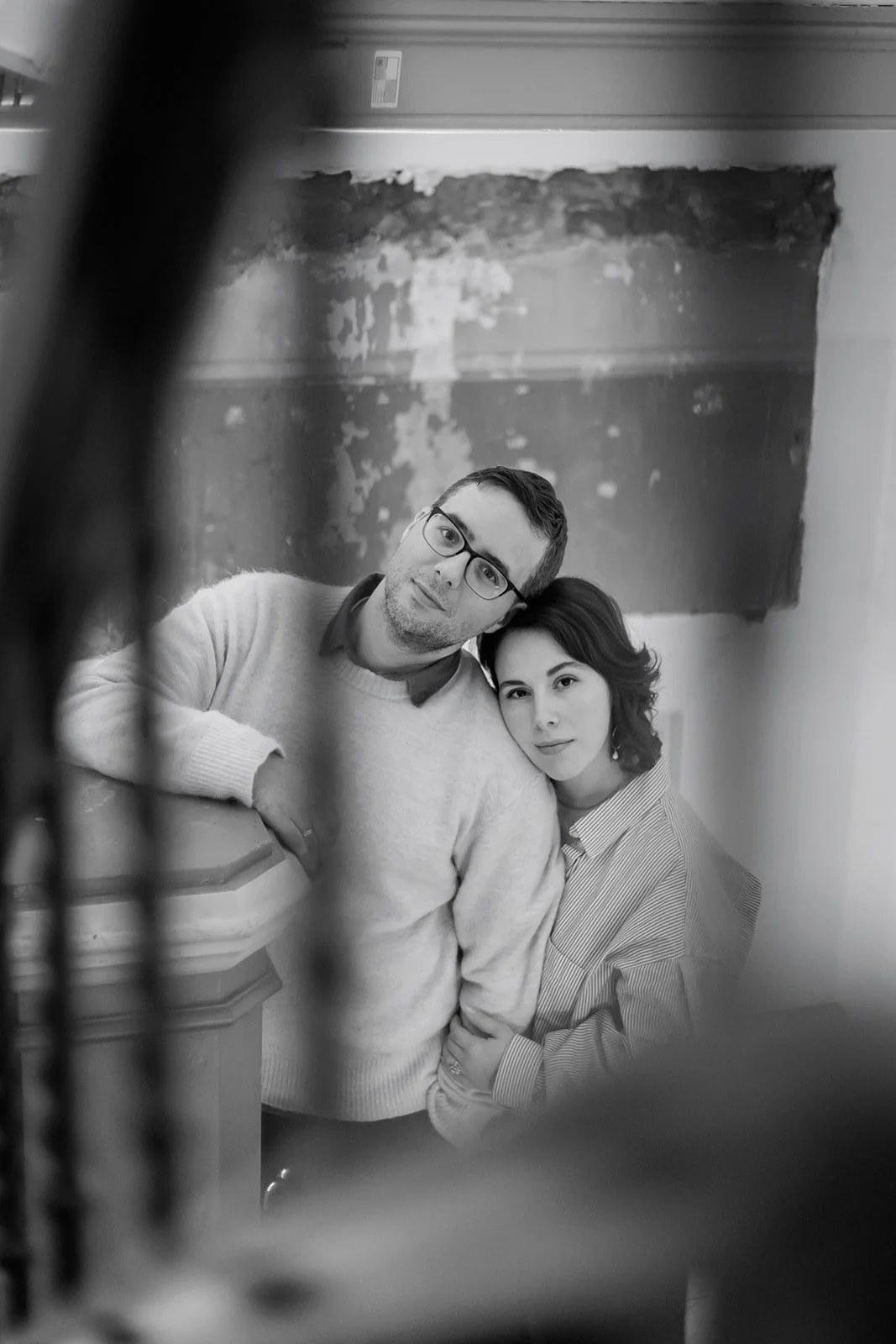 Black and white photo of a man and woman leaning on a wooden surface, looking through a mirror or a reflective surface with a textured background.