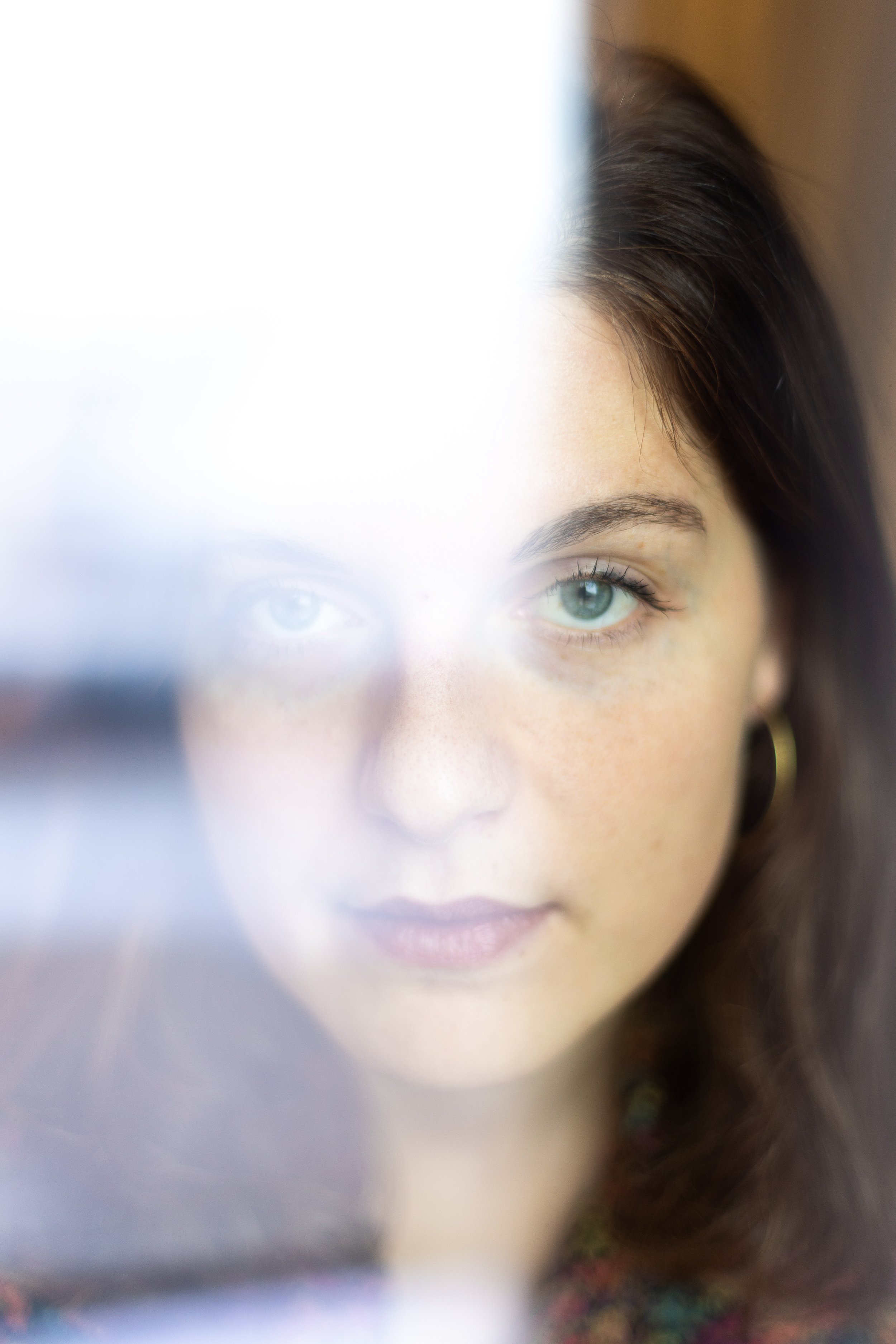 Close-up of a woman with blue eyes and dark hair looking through a semi-transparent surface, partially obscuring her face.