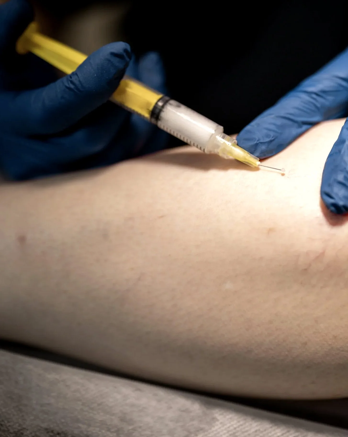 A close-up of a person receiving an injection in their arm, with a healthcare worker wearing blue gloves administering the shot.