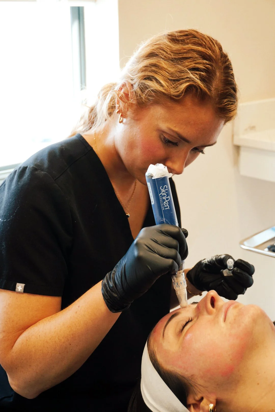 Medical professional administering a cosmetic injection to a woman lying down, with the professional holding a syringe and a cold pack.