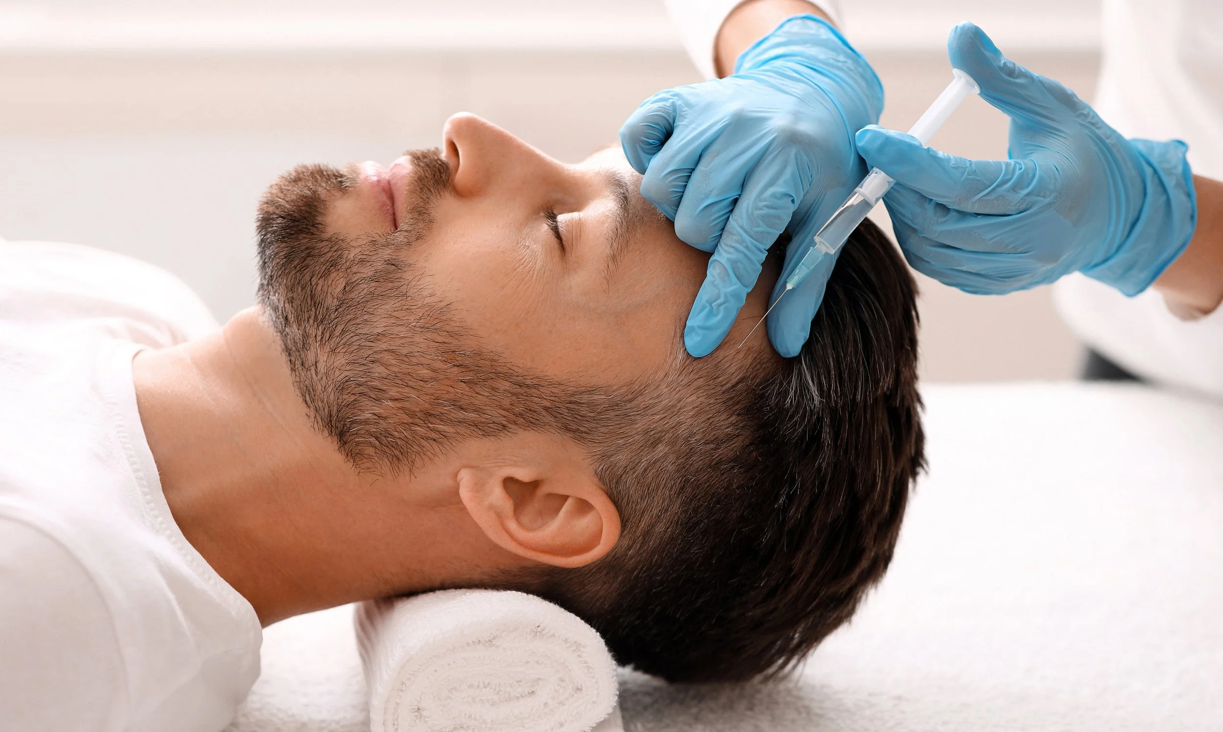 A man lying on a medical table receiving an injection in his face from a healthcare professional wearing blue gloves.