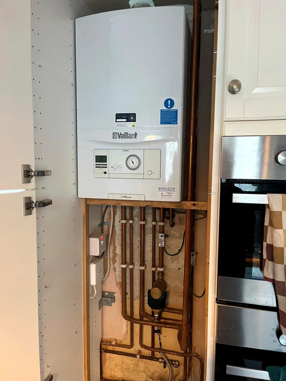 Gas boiler installed neatly inside a kitchen cupboard with organised pipework
