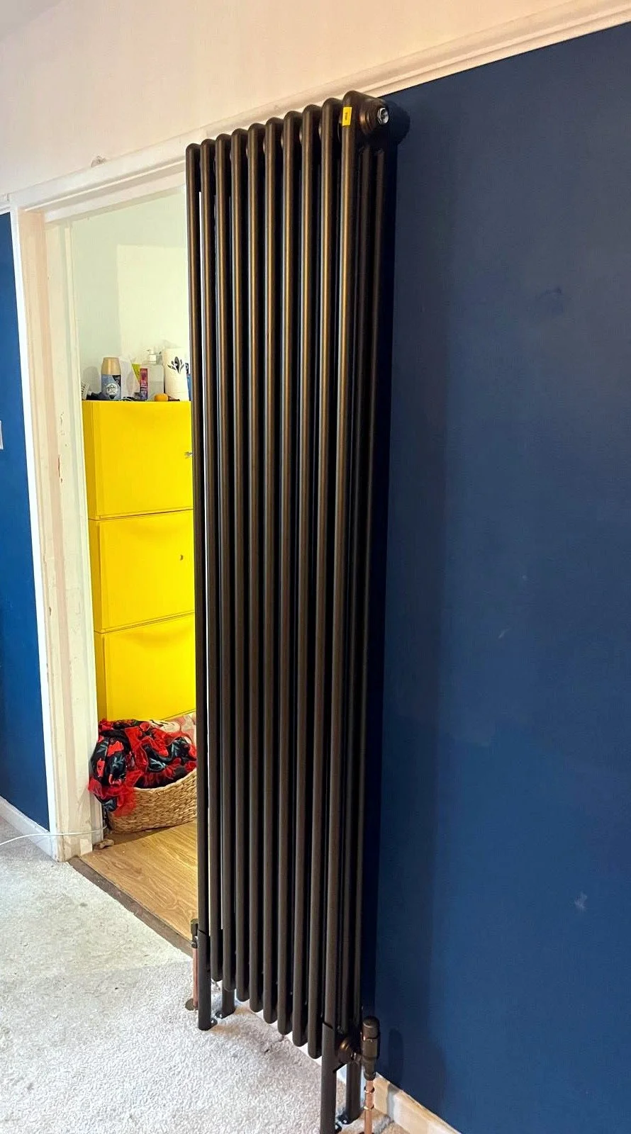 Vertical designer radiator installed neatly in a modern home interior with clean pipework and professional finish.