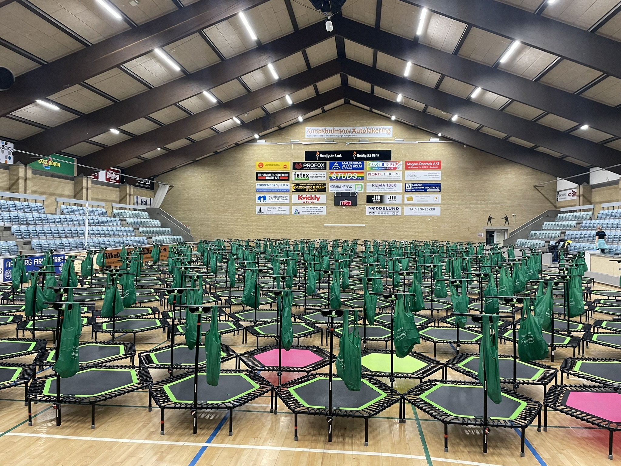Indendørs gymnastikhal med mange jump fitness trampoliner og grønne rygsække, klar til arrangement.