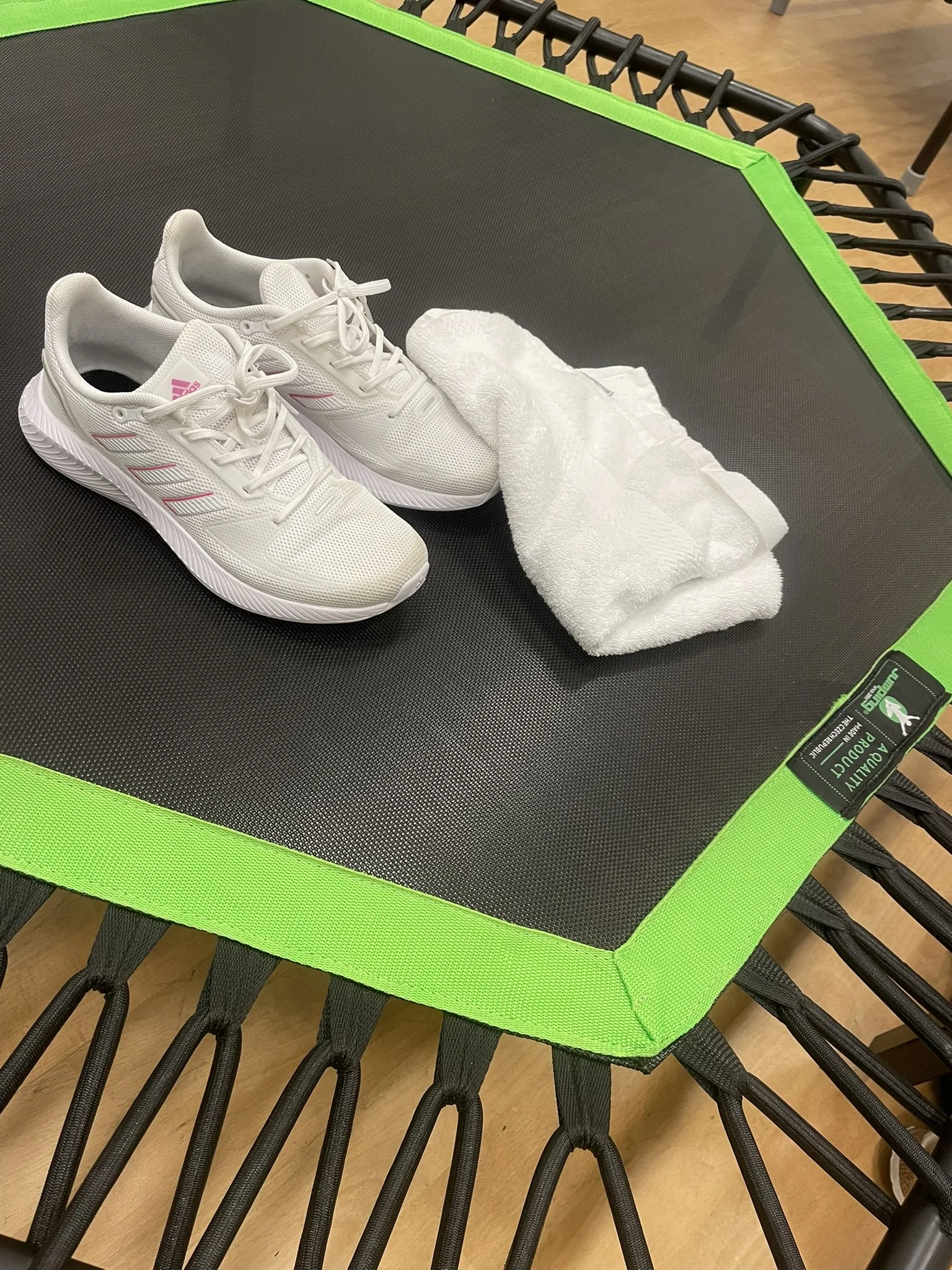 Et par hvide jump sko og et lille håndklæde på en sort jump fitness trampoline med grøn kant.