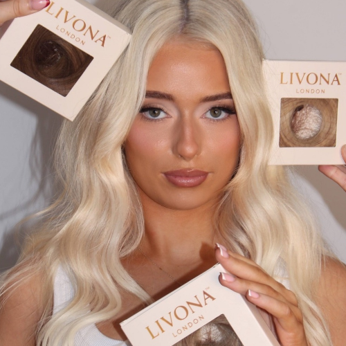 Blonde model, wearing LIVONA LONDON hair, holding three boxes of LIVONA London hair extensions