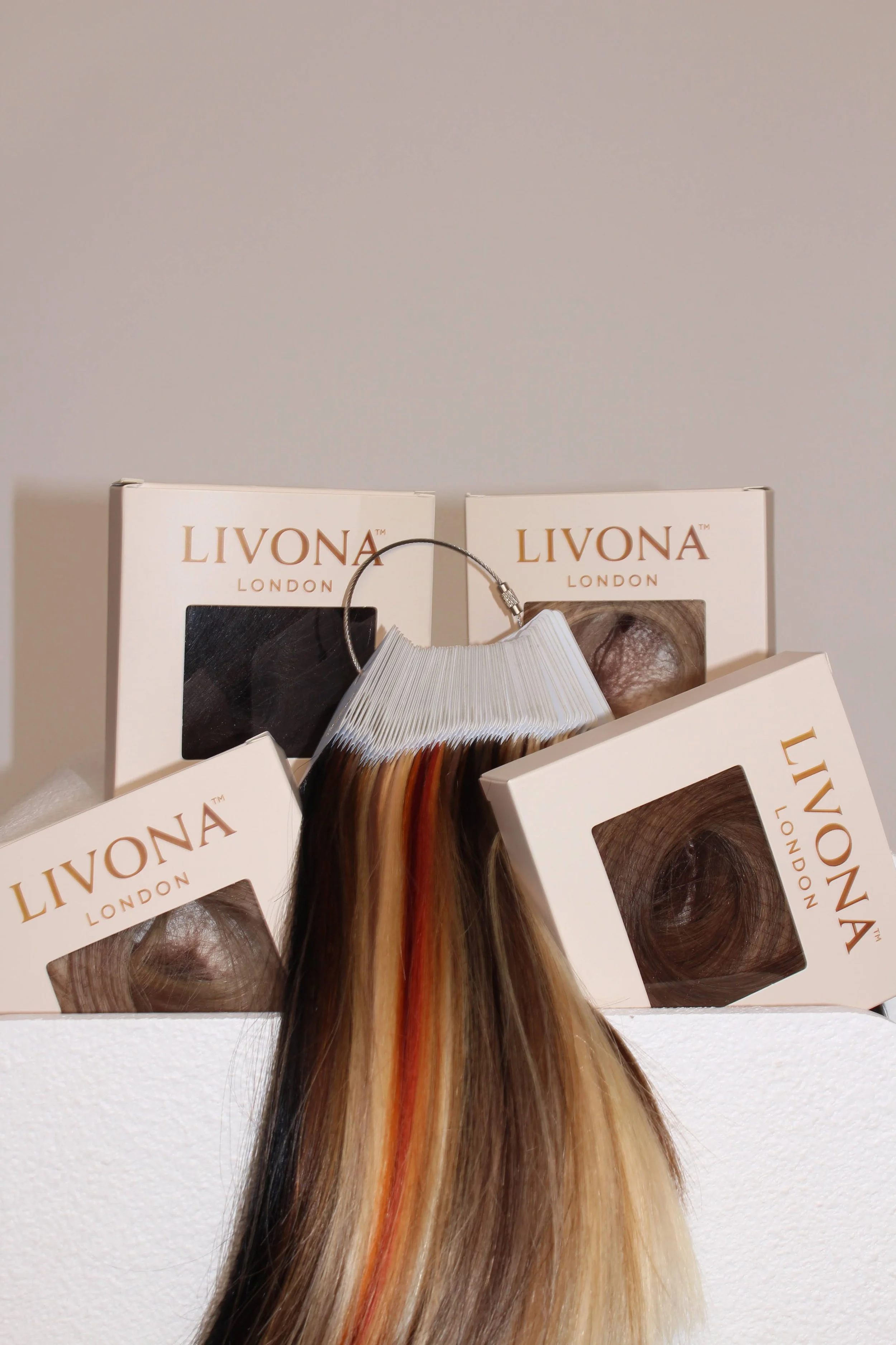 Hair color samples and hair extensions from Livona London displayed on white boxes, with a multicolored hair extension hanging in front.