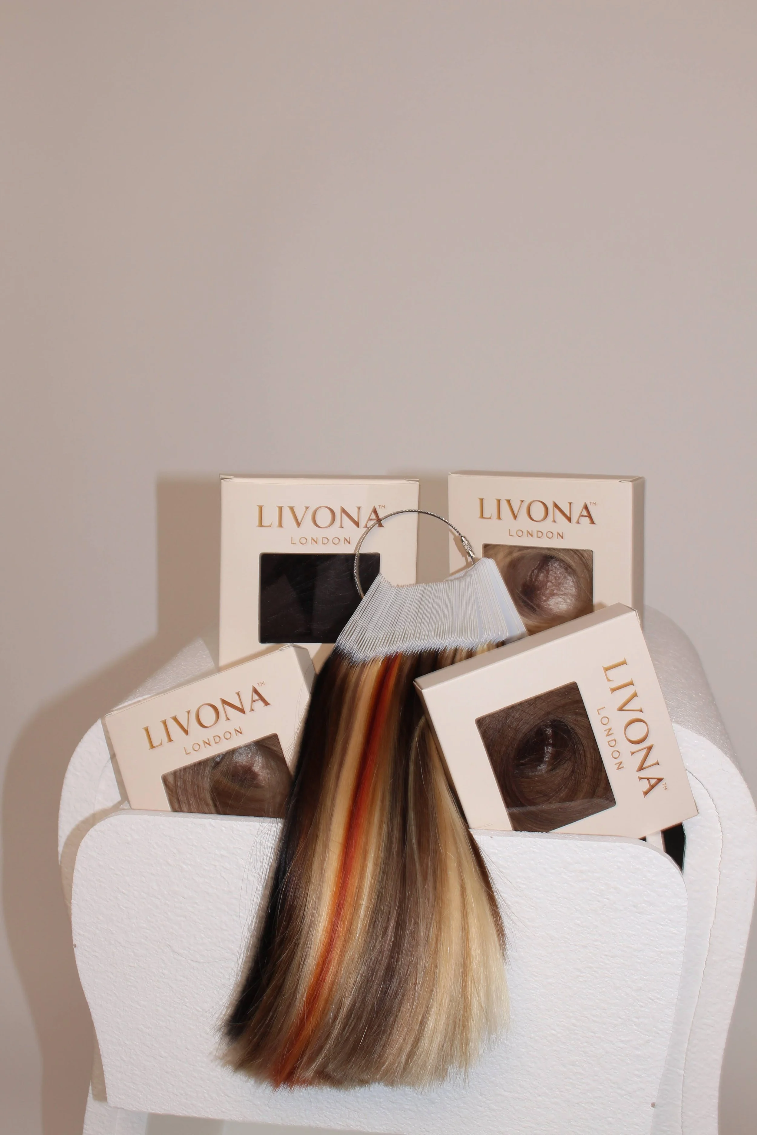 Hair extension boxes labeled Livona London with a hair sample attached, displayed on a white textured stand.