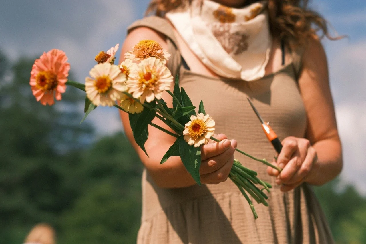 Person holding a bouquet of flowers with a pen or tool in hand, outdoors with a blurred natural background.
