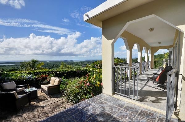 View from a balcony showing outdoor seating and a lush green landscape with views of the ocean.