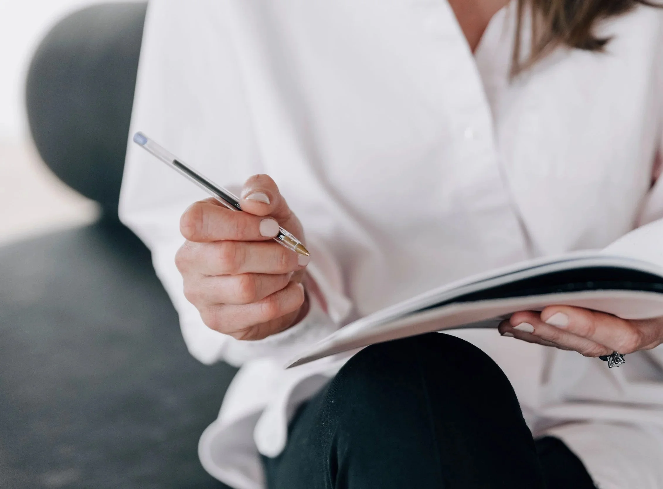 Close-up of a woman holding a pen and a notebook, sitting with one knee up.