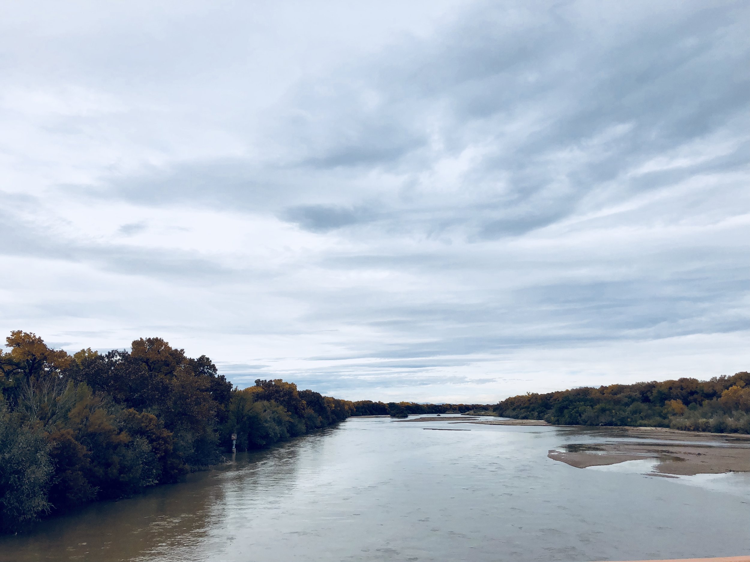 A river flowing through a landscape with trees on both sides, under a cloudy sky.