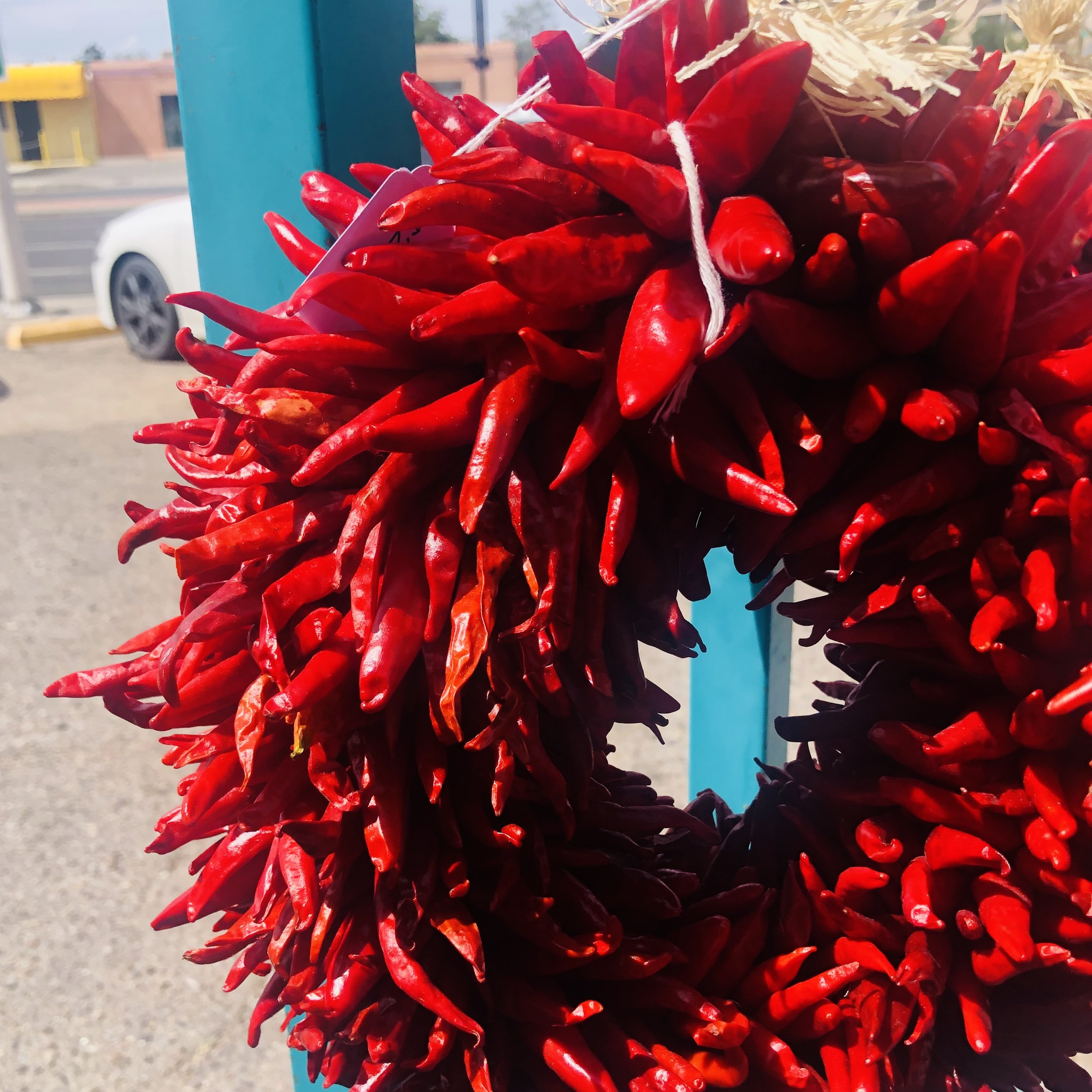 Close-up of a bright red chili pepper wreath hanging outdoors against a blue post.