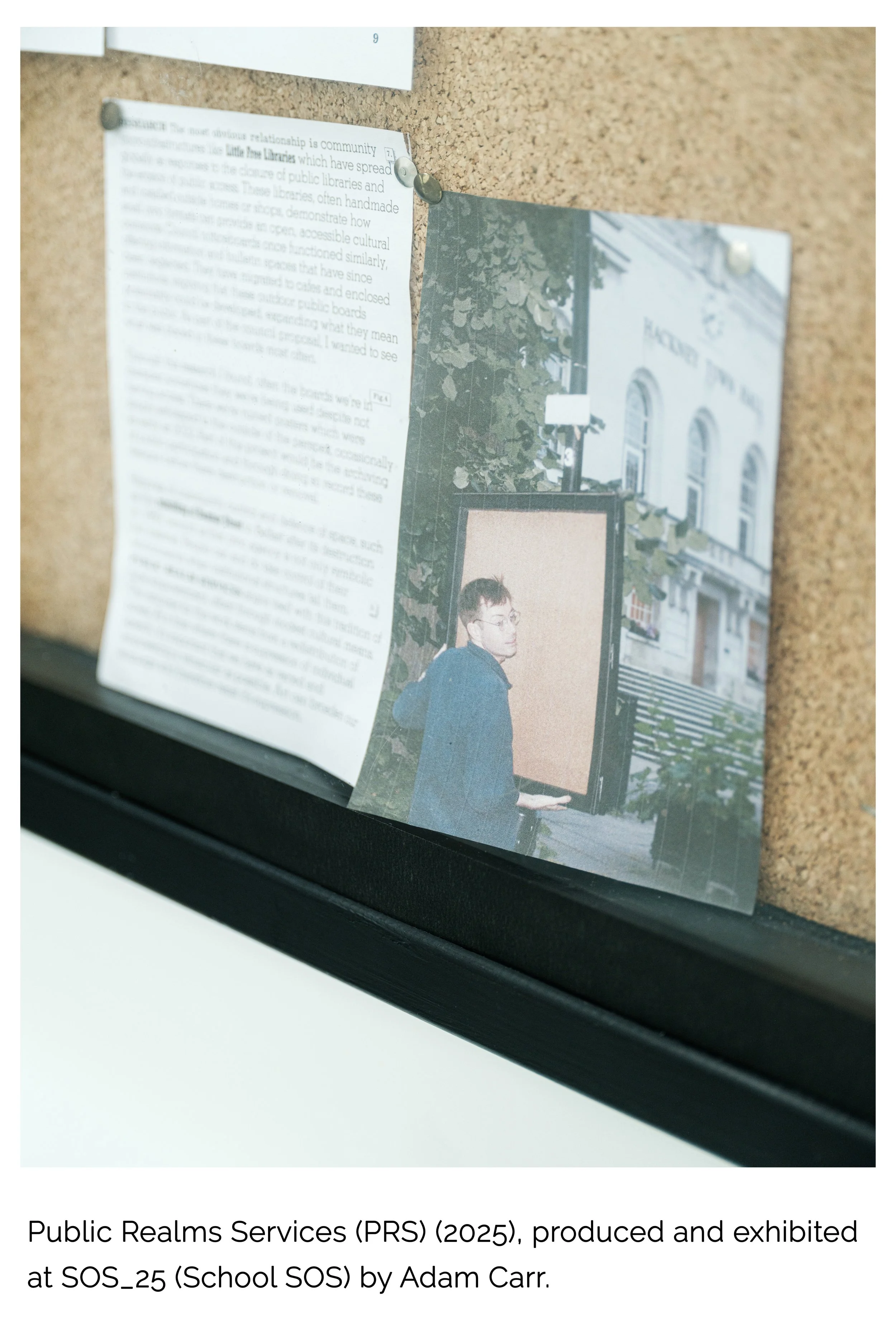 A bulletin board with pinned papers and photographs, showing a person with glasses looking to the side, standing outside in front of a white building with arched windows.