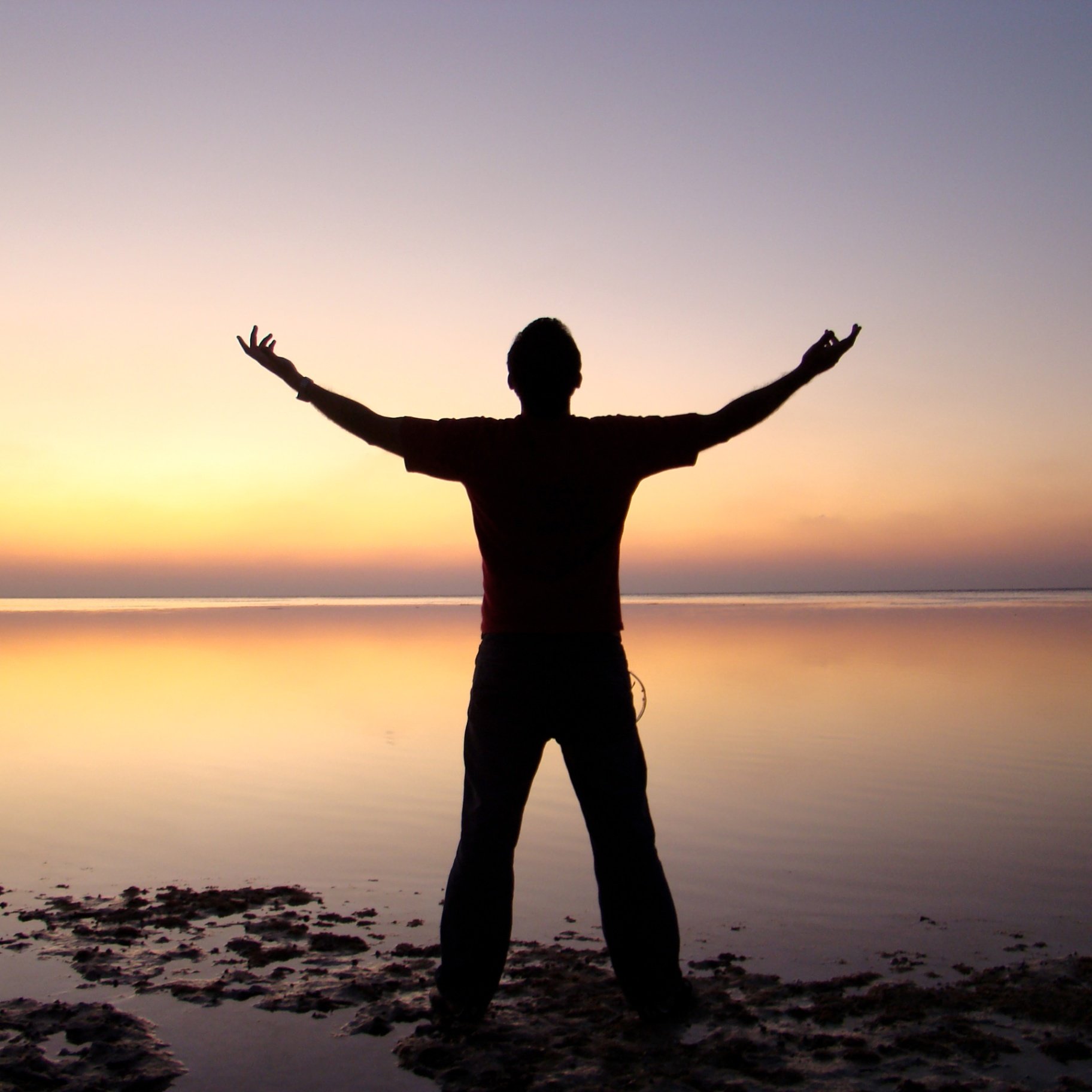 Person standing on beach at sunset with arms outstretched.