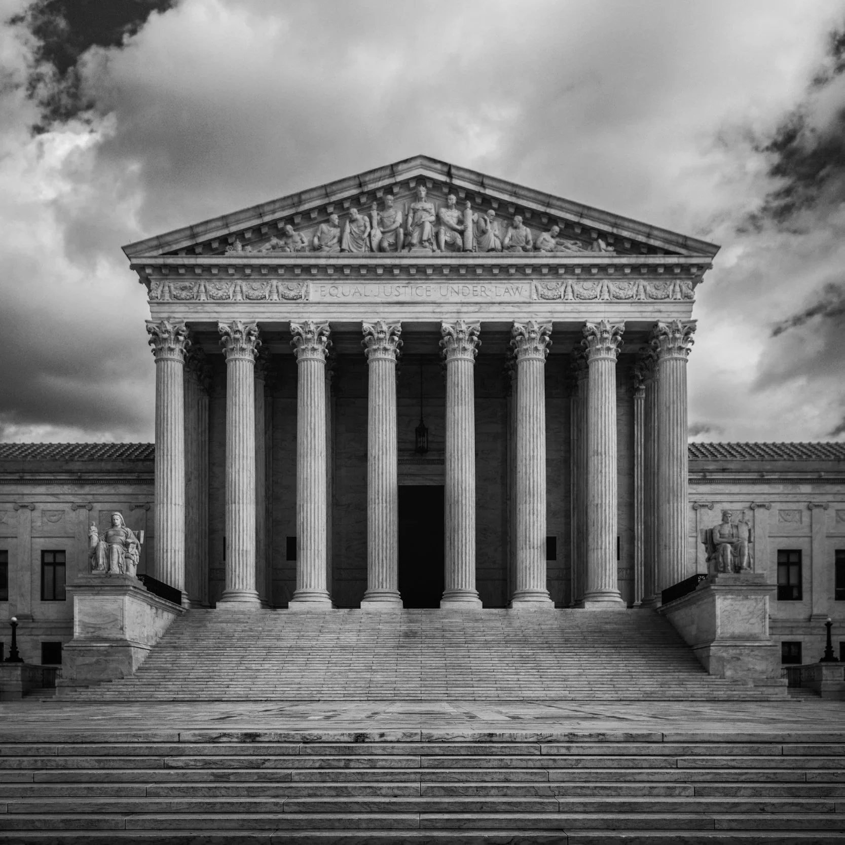 Black and white photograph of the U.S. Supreme Court building with columns, statues, and steps under a cloudy sky.