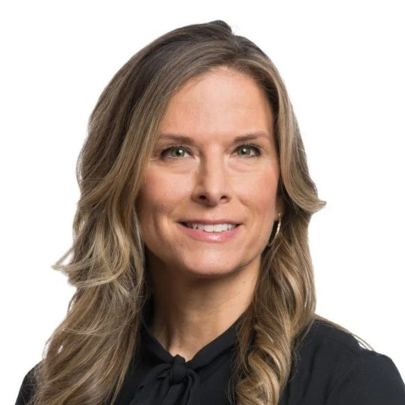 Portrait of a smiling woman with long, wavy blonde hair, wearing a black top, against a plain white background.