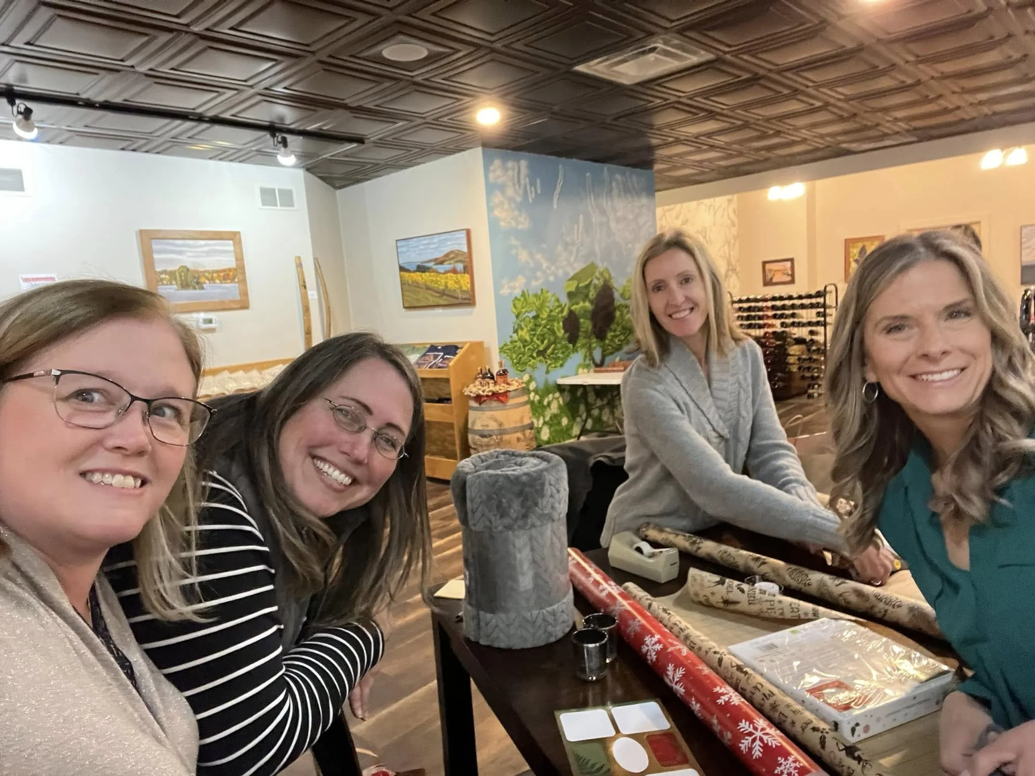 Four women smiling and wrapping presents at a table.