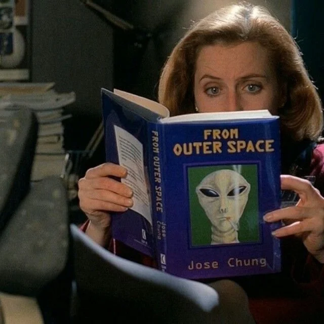 Gillian Anderson as Dana Scully reading a book titled From Outer Space in a scene from The X-Files.