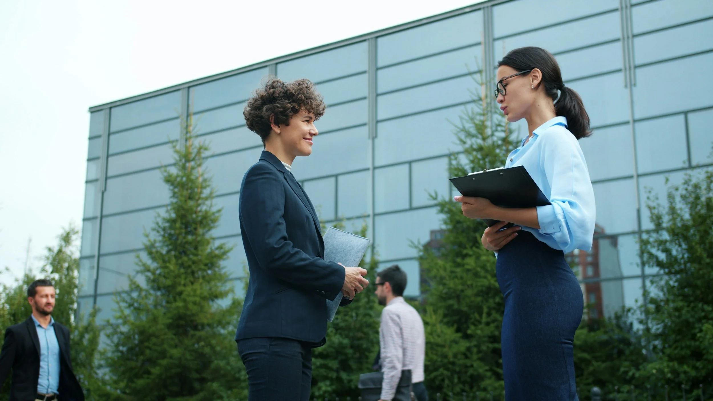Two young women standing outside an office building wearing business outfits.