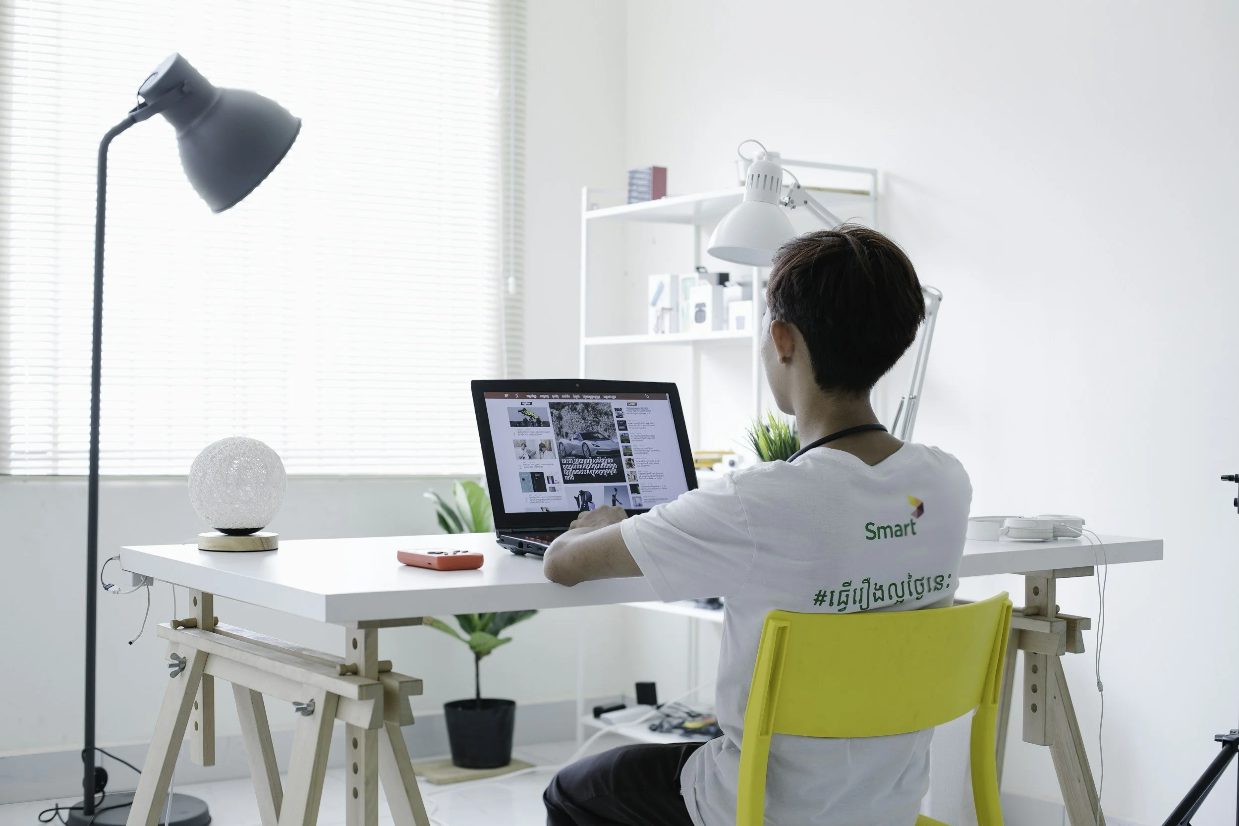 A person browsing the Internet on a laptop, sitting on a yellow chair, at a white desk.