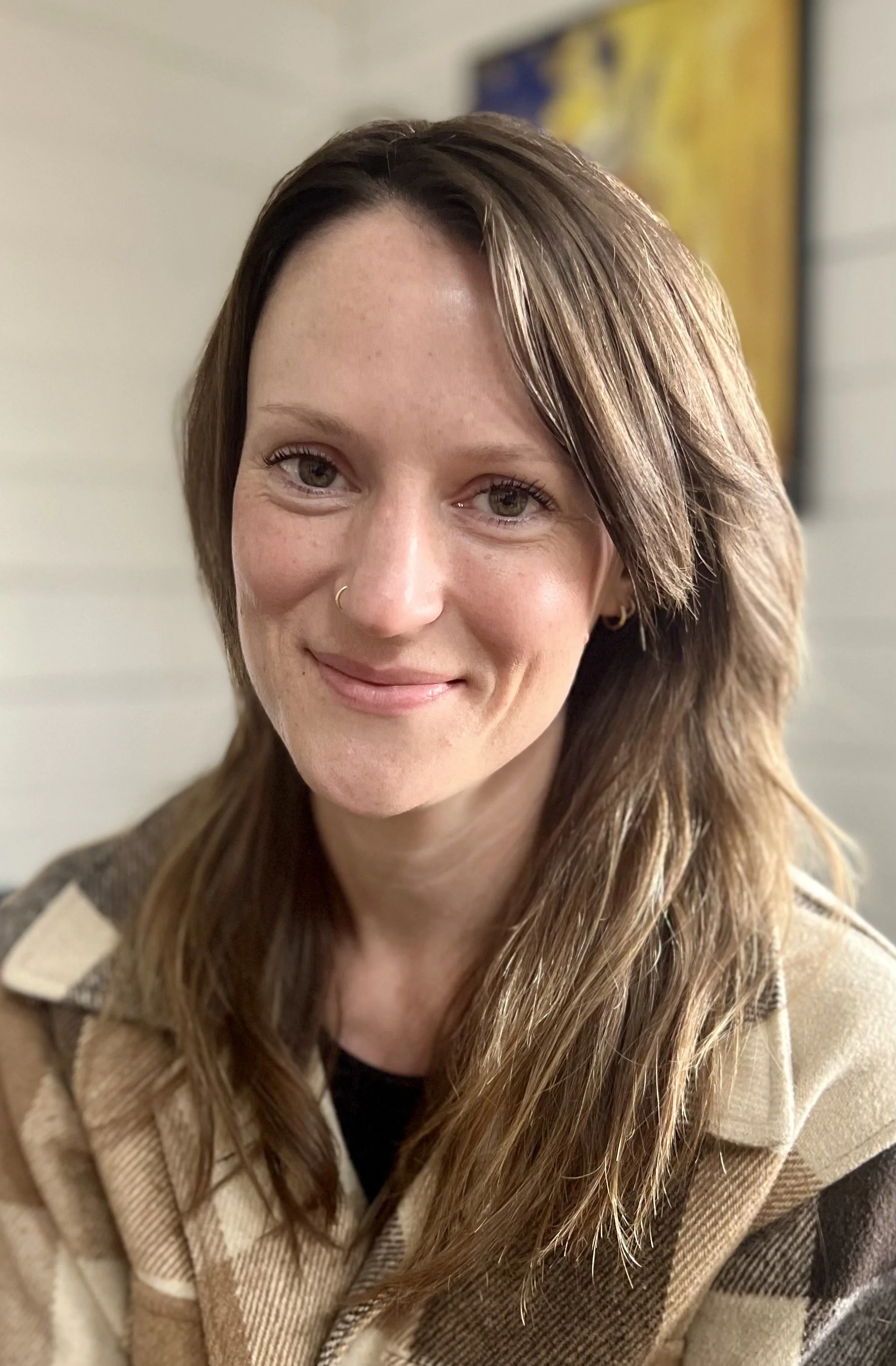 A woman with shoulder-length brown hair, wearing a beige and black plaid jacket, smiling at the camera.