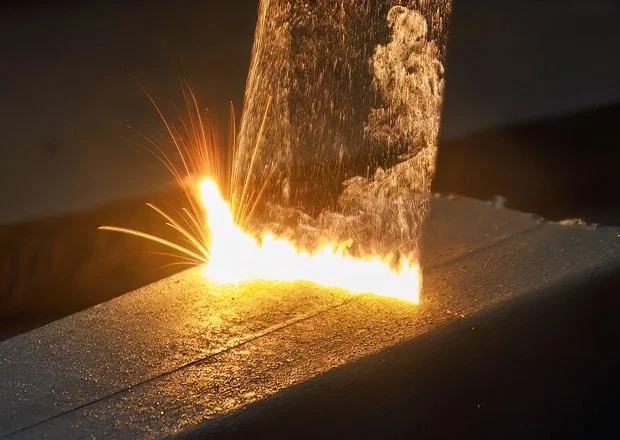 A metal cutting process using a plasma torch, creating sparks and bright light as it cuts through a metal workpiece.