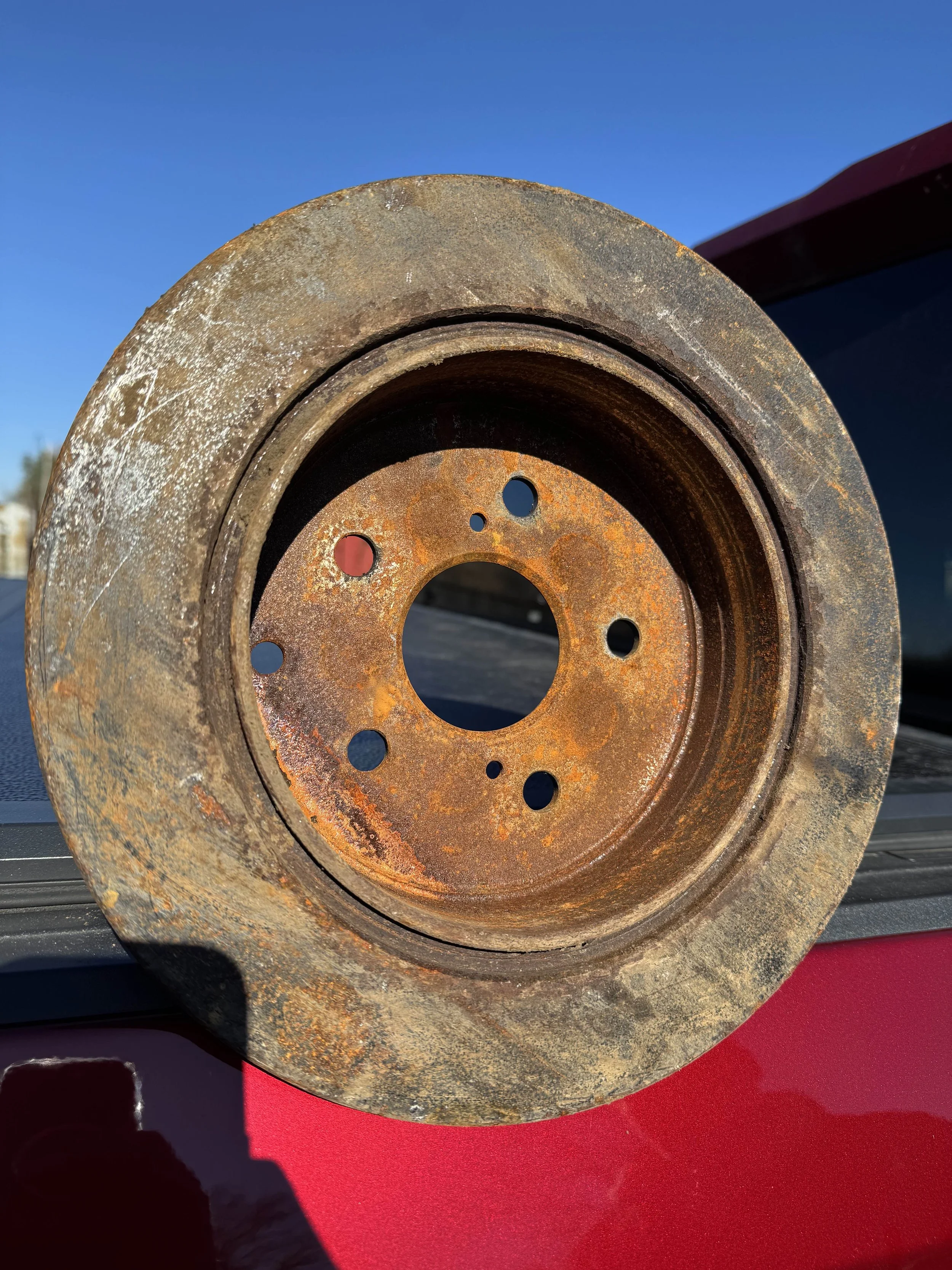 Close-up of a rusty, used metal wheel or pulley resting on a surface outdoors under clear blue sky.