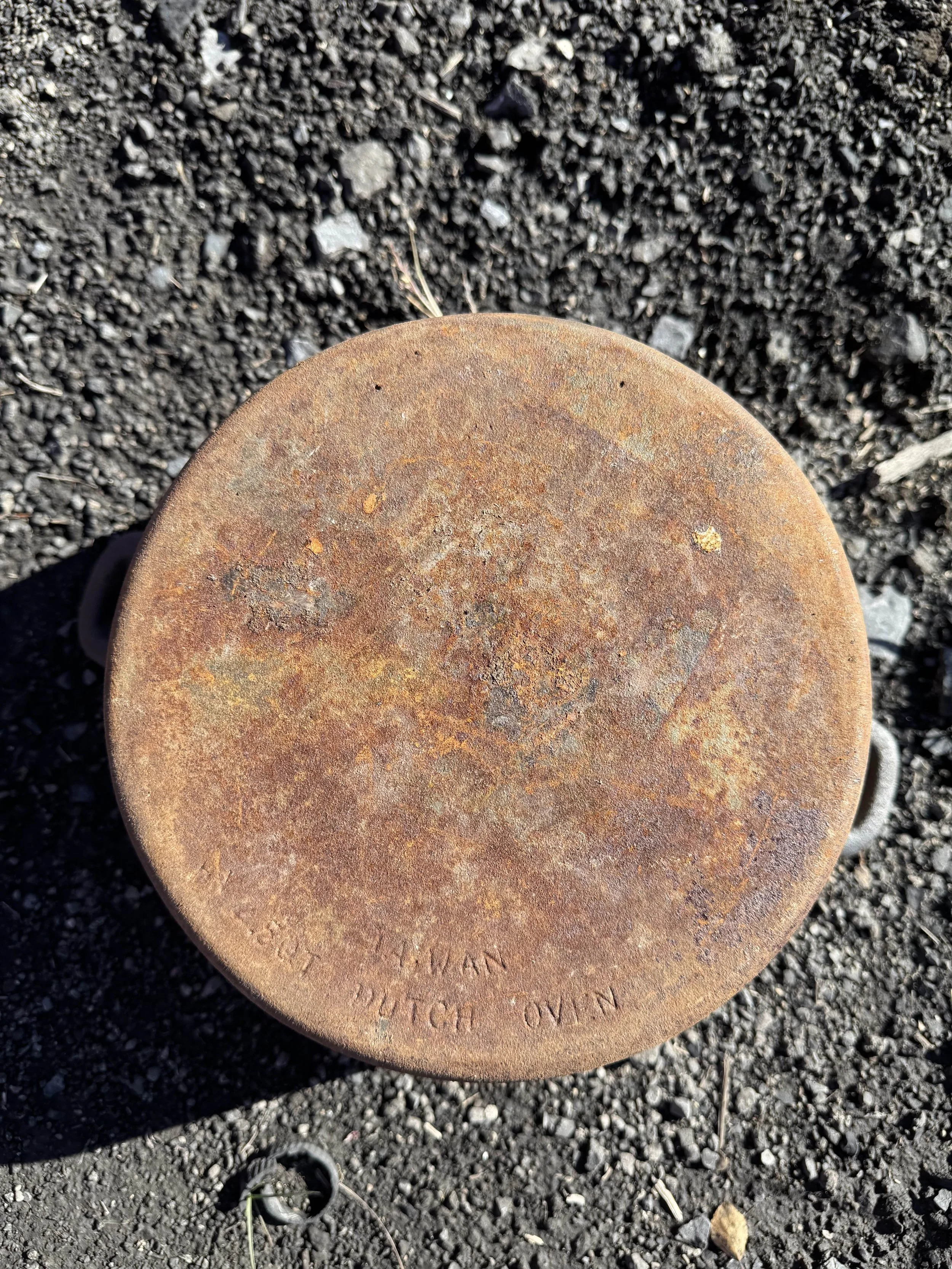 Top view of a rusty, round metal object on the ground with gravel and small rocks around it.