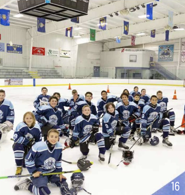 Group of young ice hockey players in blue jerseys posing on an ice rink with hockey sticks and helmets.
