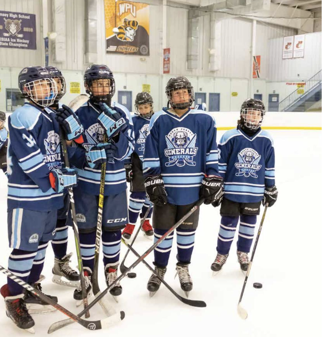 A group of young ice hockey players wearing blue and black uniforms and helmets, standing on the ice rink during a game or practice session.