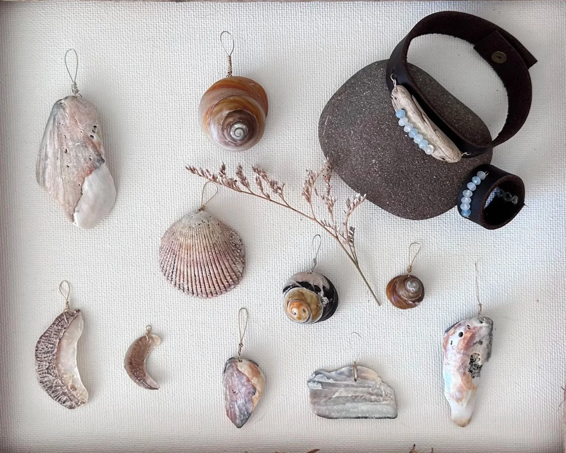 Collection of seashells, a stone, a branch, and jewelry pieces with beads on a white background.