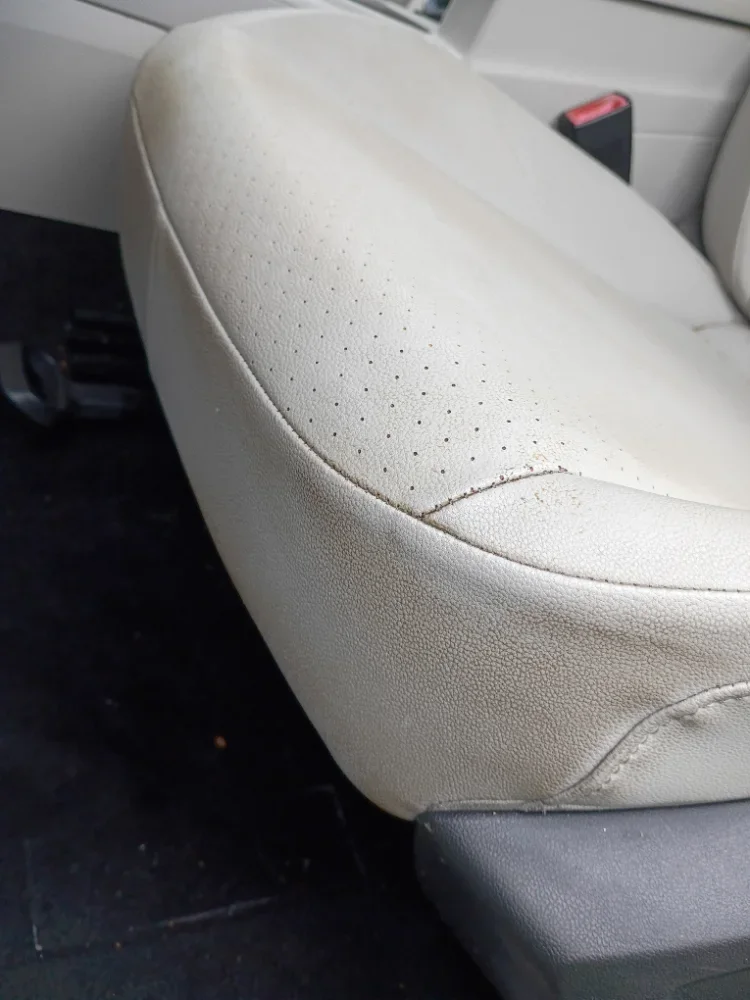 Close-up of a beige leather car seat with visible wear and small tears, in a vehicle interior.