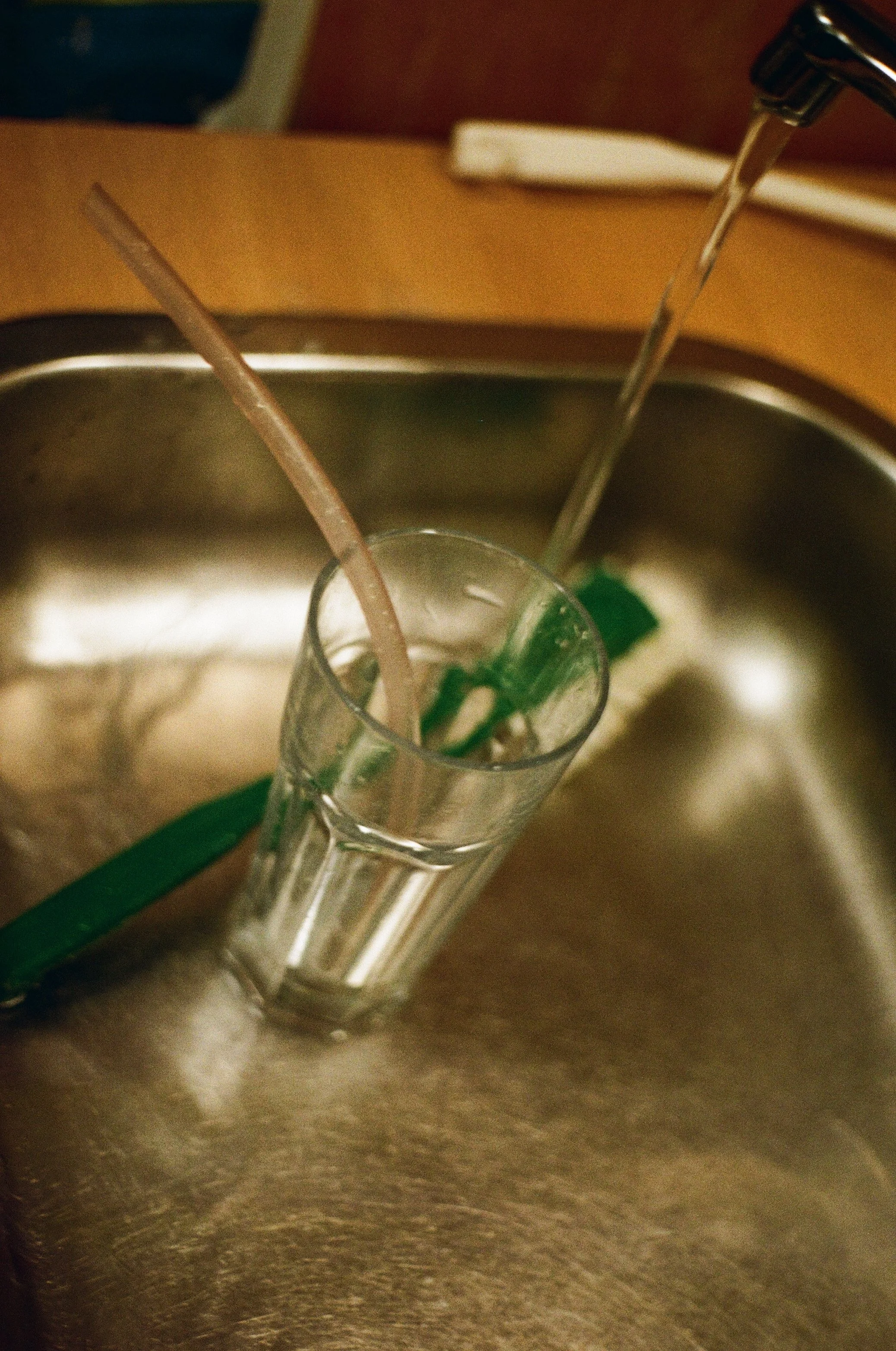 Brukt glass i vasken med hjemmelagd sugerer oppi. kranen står på og det renner vann på siden. Det er også en grønn oppvaskbørste