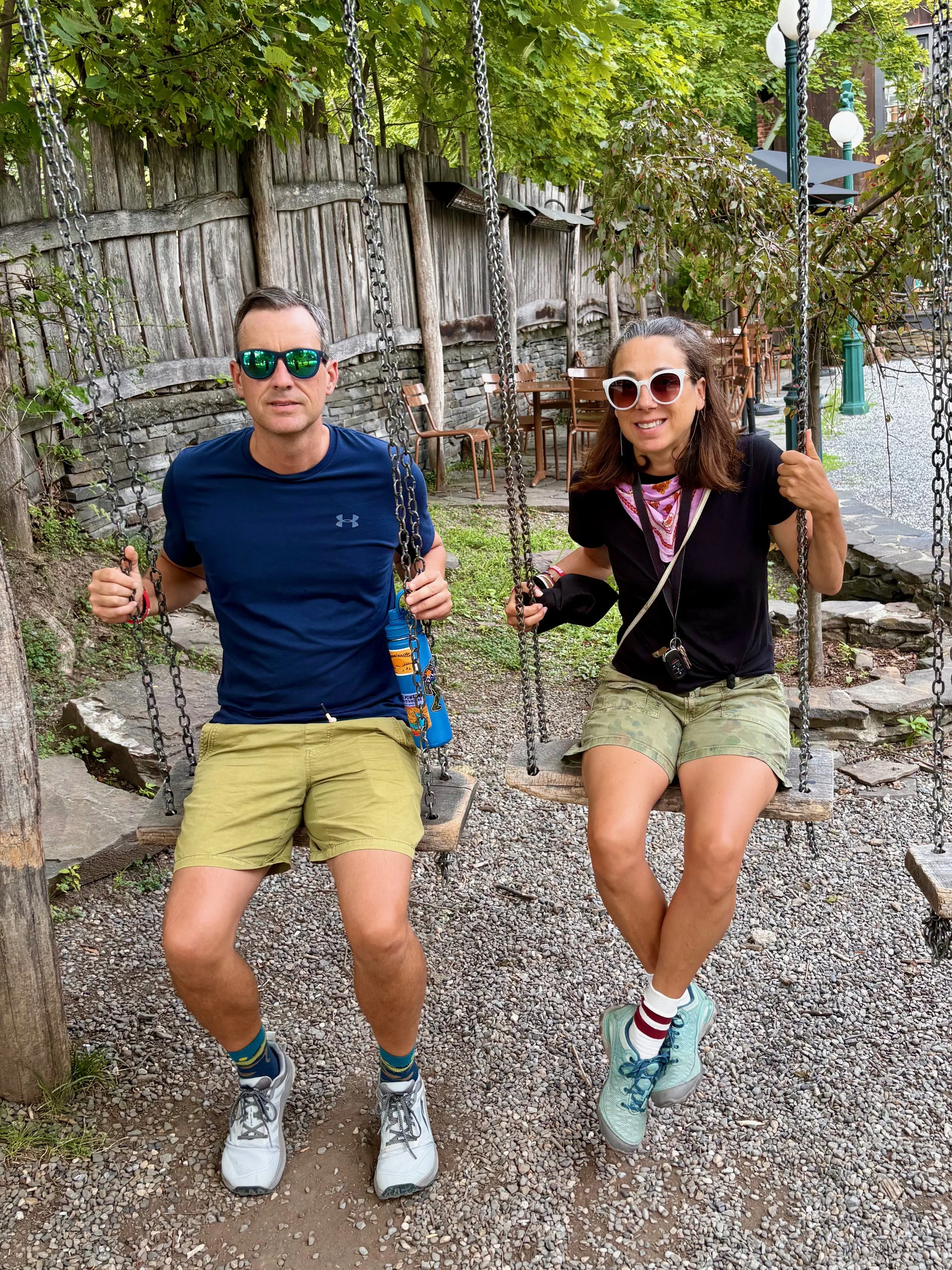 Roberta and her husband sitting on swing seats in an outdoor park area. Woodstock, New York