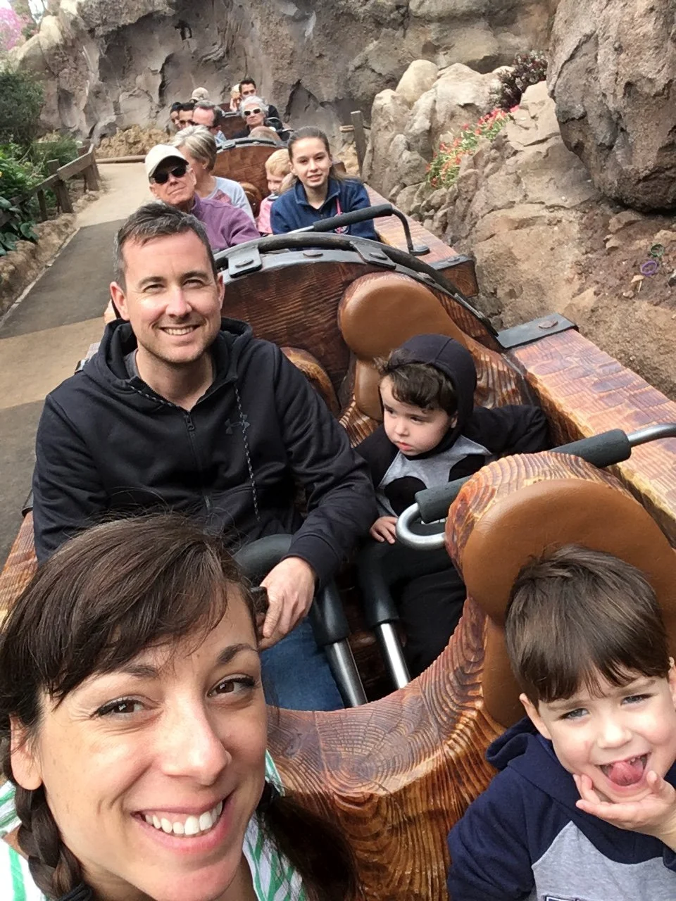 Roberta and her family riding a wooden log flume ride through a rocky outdoor setting at an amusement park. Snow White and the Seven Dwarfs Mine Train Magic Kingdom