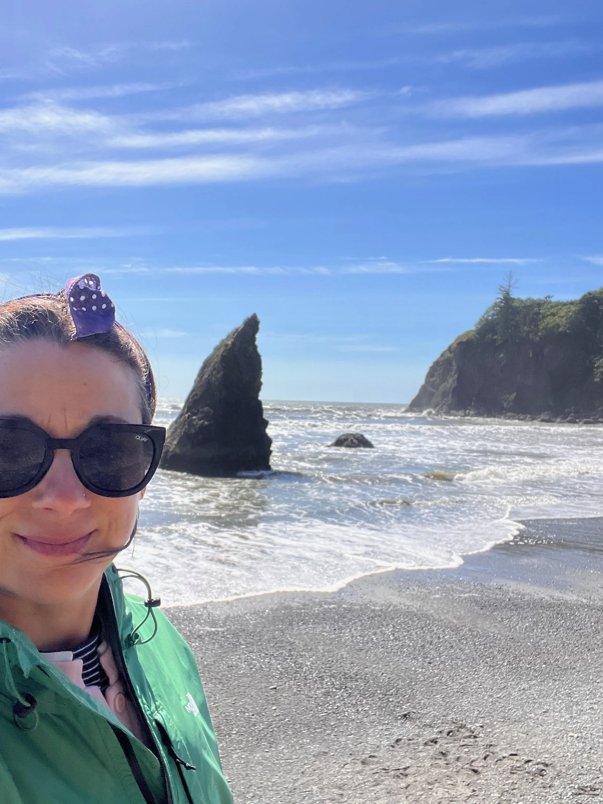 Roberta at a beach with large rock formations, blue sky, and ocean waves. Ruby Beach Washington