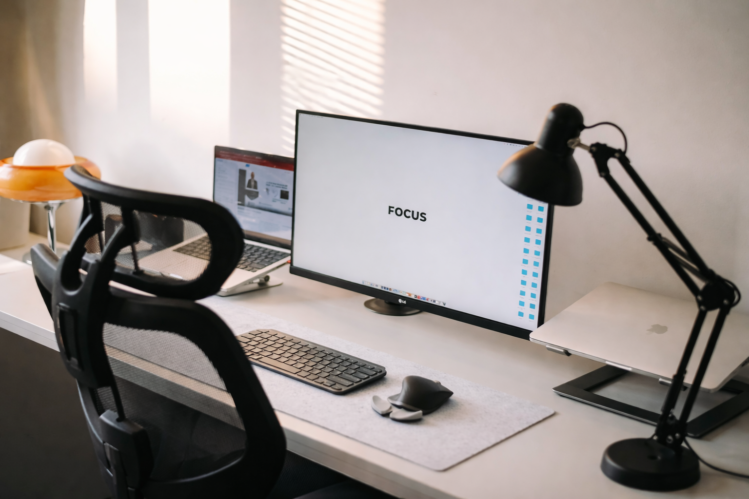 Bureau avec deux écrans, clavier, souris, lampe de bureau, ordinateur portable, chaise de bureau, et une lampe orange avec une boule blanche.