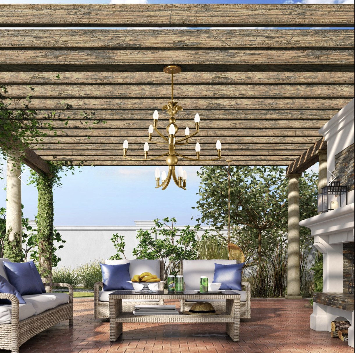 Outdoor patio with wicker furniture, blue cushions, a coffee table with snacks and drinks, greenery, and a chandelier under a wooden pergola.