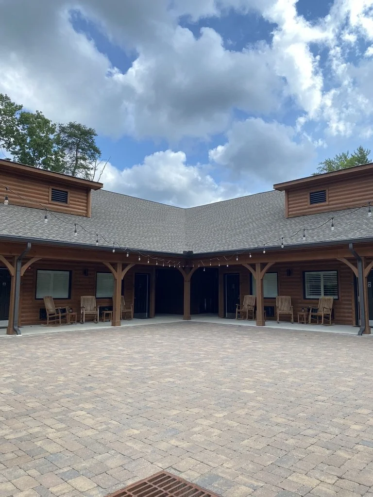 The wooden Lodge with a V-shaped courtyard featuring rocking chairs, string lights, and a cobblestone patio
