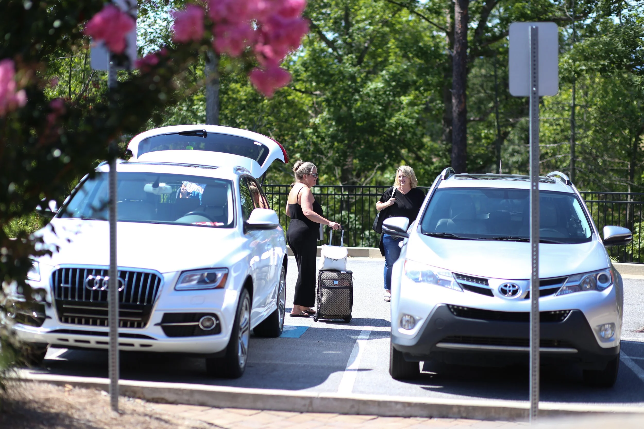 Two women who just arrived to retreat, talking by their cars while unloading their suitcases