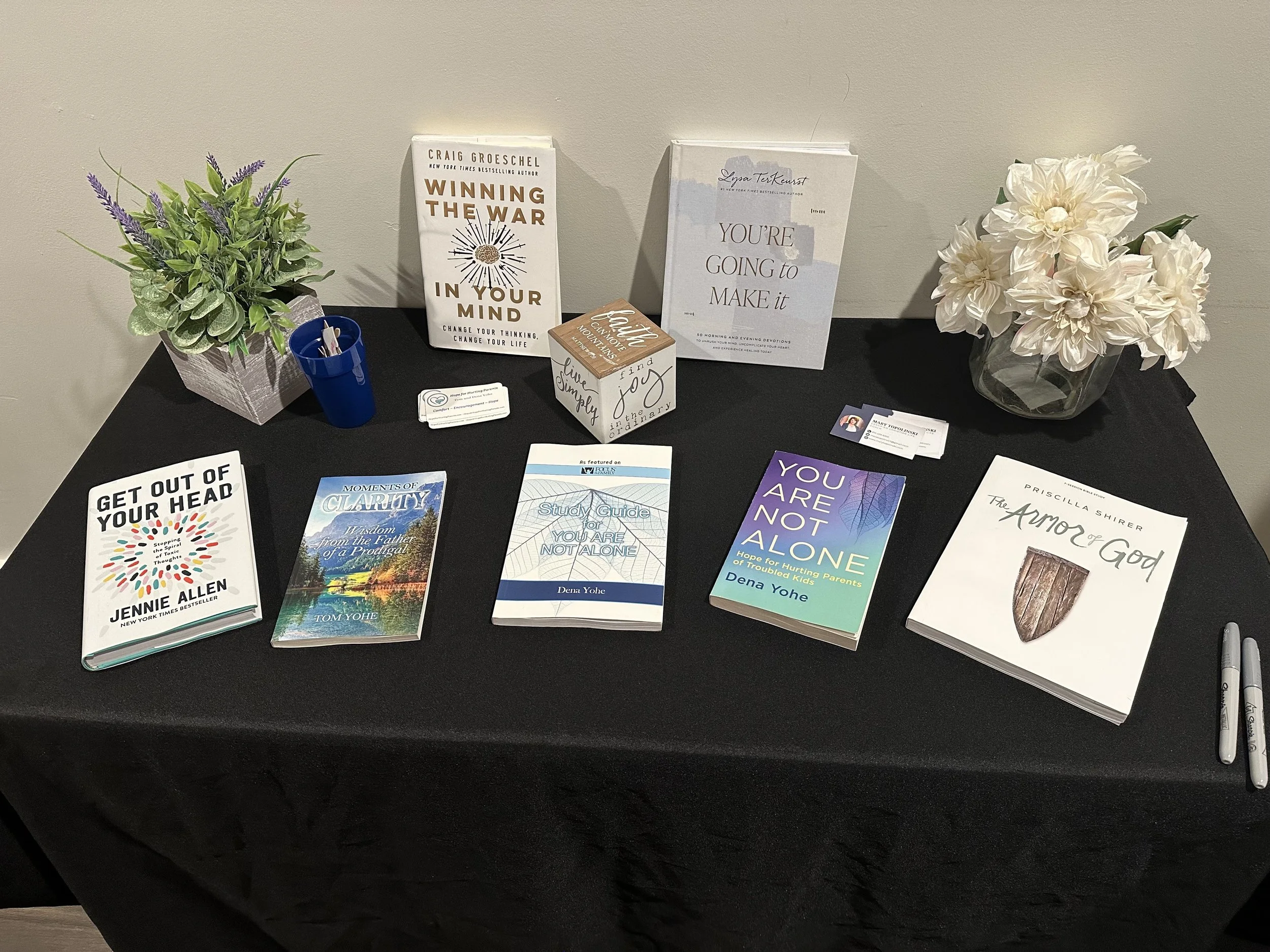 A resources table at a Just Be Held retreat with several books displayed on a black tablecloth
